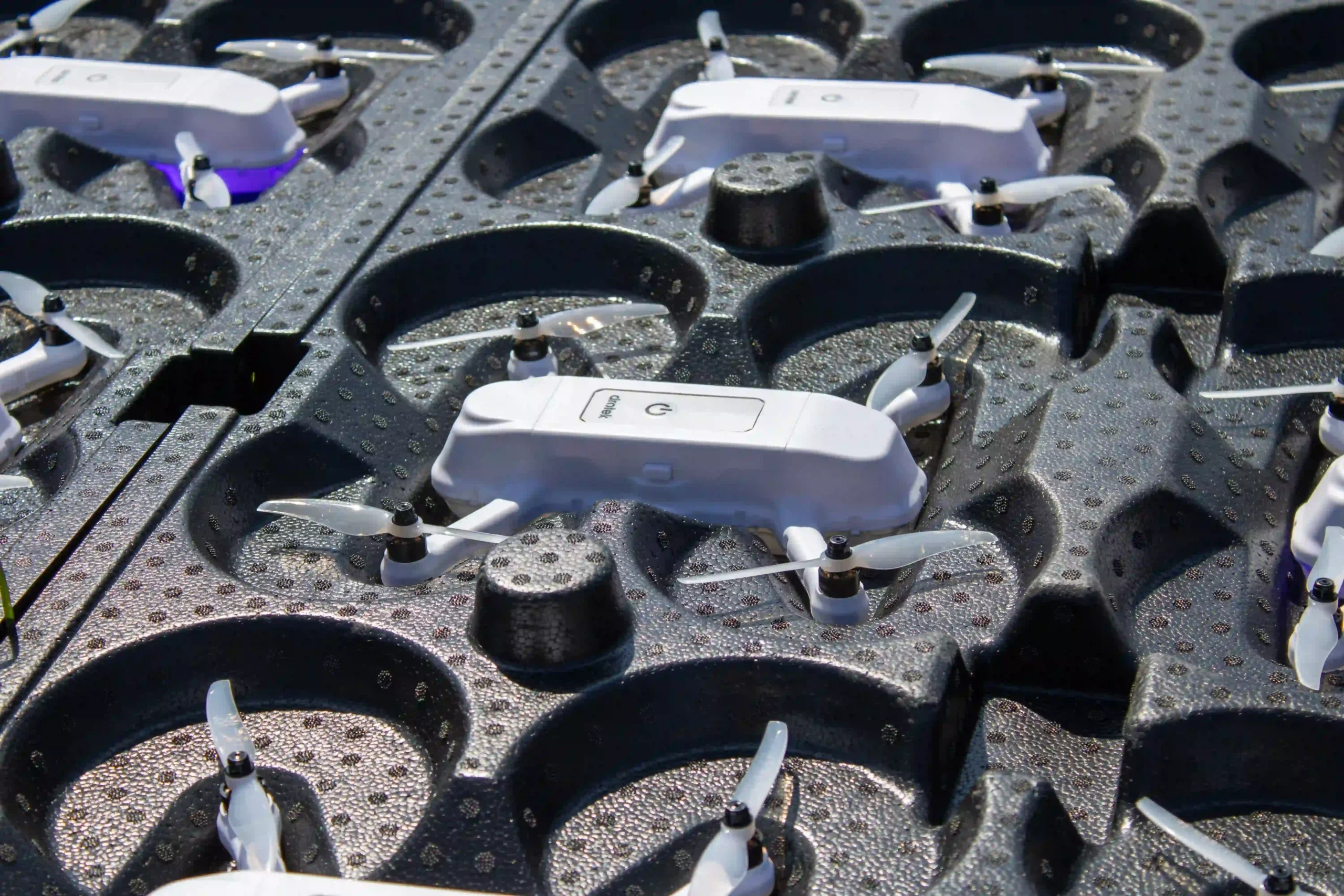 White drone light show drones stored in black transport trays before deployment. The compact LED-equipped quadcopters are organized for transportation and fleet management, showcasing professional drone show technology.