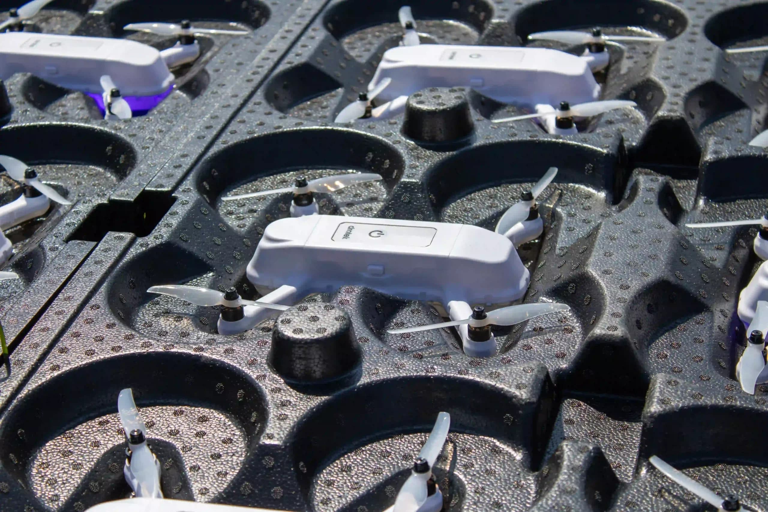 White drone light show drones stored in black transport trays before deployment. The compact LED-equipped quadcopters are organized for transportation and fleet management, showcasing professional drone show technology.